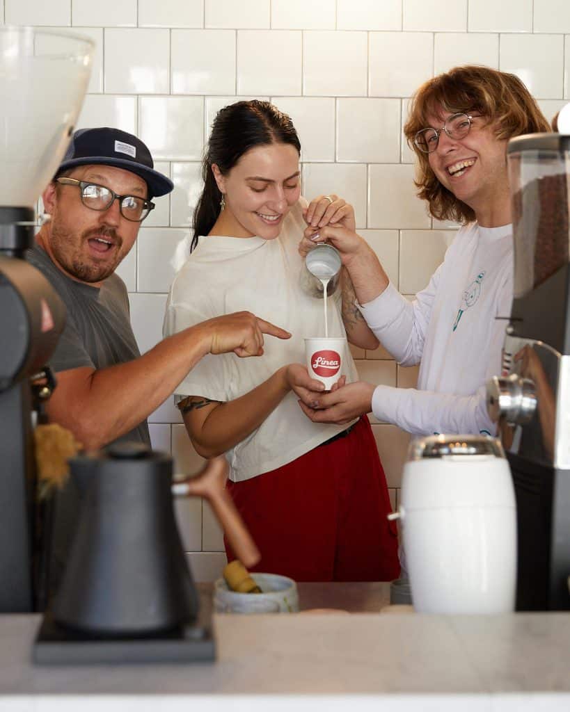 Three team members smiling and pouring milk into to-go mug.